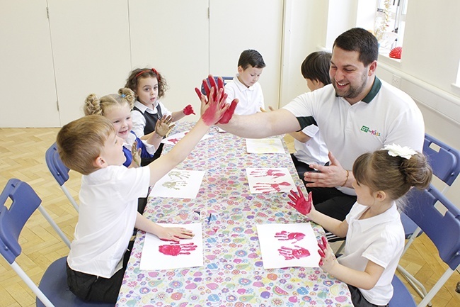 Therapist high fiving a child with painted hands, other children watching and pressing hands onto paper